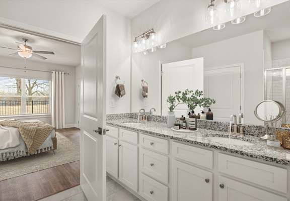 A bathroom with a large mirror, a sink, and a bedroom with a window.