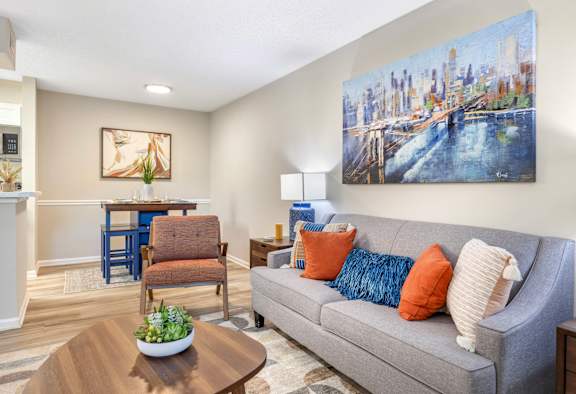 A living room with a grey couch, a coffee table, and a painting of a cityscape on the wall.