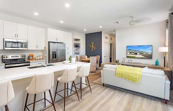 A modern kitchen with white countertops and a white sofa with a yellow throw.
