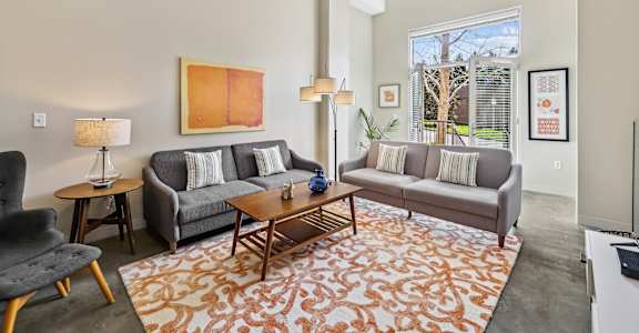 A living room with a grey couch, a black chair, a wooden coffee table, and a painting on the wall.