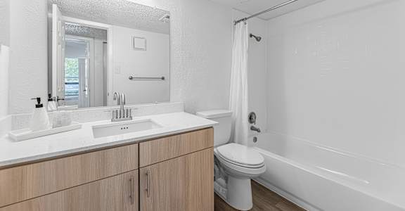 A white bathroom with a sink, mirror, toilet, and bathtub.