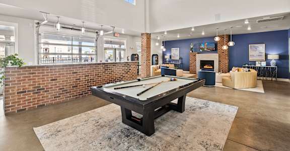 A pool table is in the middle of a room with a brick wall.