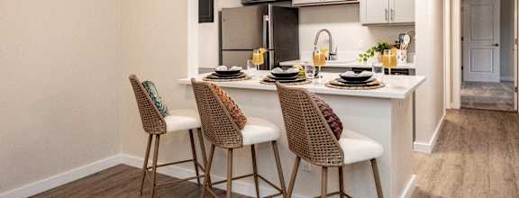 A kitchen with a white countertop and brown chairs.