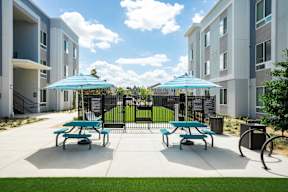 A sunny day at a residential complex with picnic tables and umbrellas.