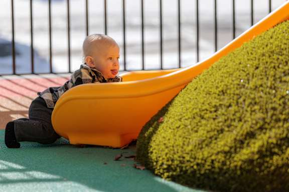 A baby is sitting in a yellow bathtub next to a green bush.