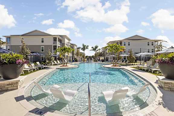 A large outdoor pool with a waterfall and lounging chairs.at Verity Luxury Apartments, Vero Beach, FL 32960