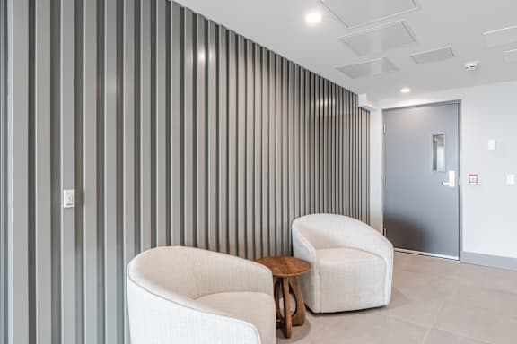 A room with a white chair and a grey striped wall.