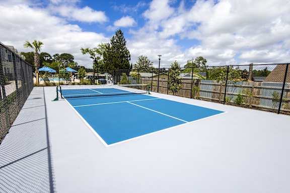 A tennis court with a blue surface and white lines, surrounded by a fence and trees.