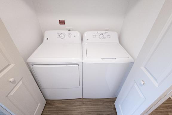 A pair of white front loading washing machines in a small laundry room.