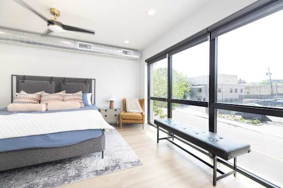 A bedroom with a bed, chair, and window overlooking a street.