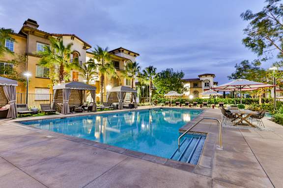 A swimming pool surrounded by lounge chairs and umbrellas at dusk at Capriana at Chino Hills, California, 91709