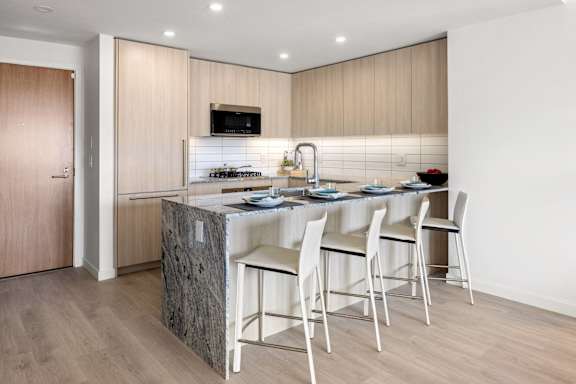 A kitchen with a granite island and white chairs.