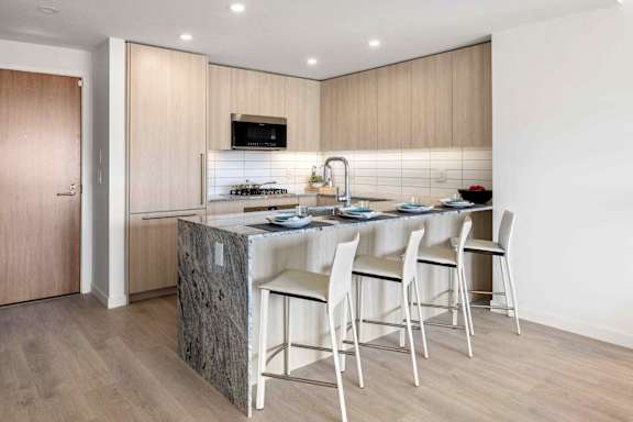 A kitchen with a granite island and white chairs.