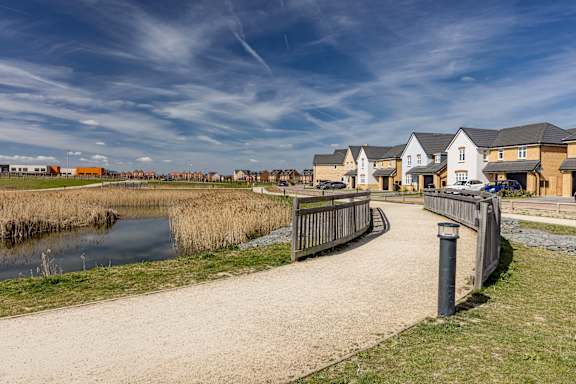 A pathway with a fence and a body of water in front of houses.