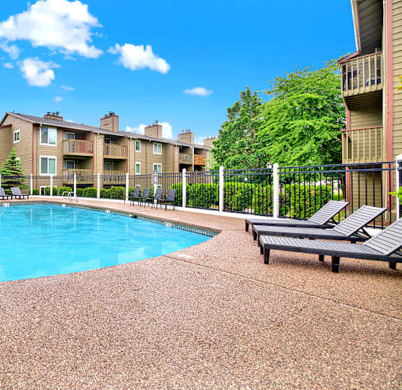 A pool surrounded by a fence and chairs.