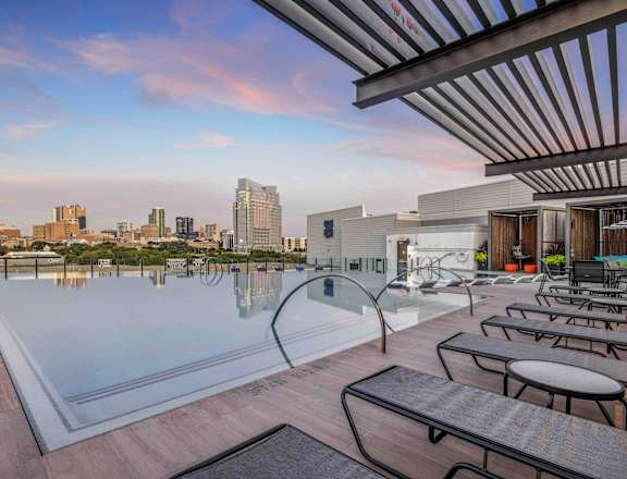A rooftop pool area with lounge chairs and a city skyline in the background.