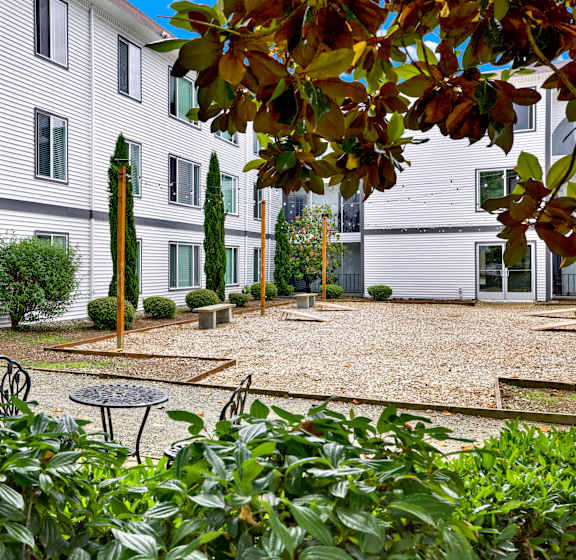A white building with a gravel courtyard and a tree with a brown trunk.