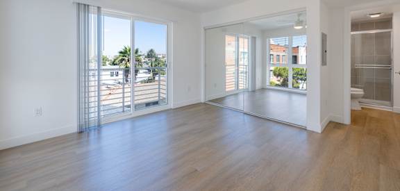 A spacious room with a ceiling fan and sliding glass doors leading to a balcony.
