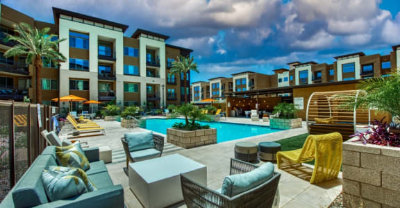 A poolside area with lounge chairs and a pool in front of apartment buildings at Elevation San Tan, Gilbert, AZ, 85295