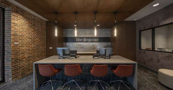 A conference room with a long table and chairs, a computer, and a sign that reads "The Register.".