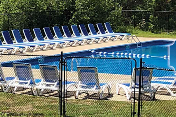 A pool surrounded by blue lounge chairs and a black fence.