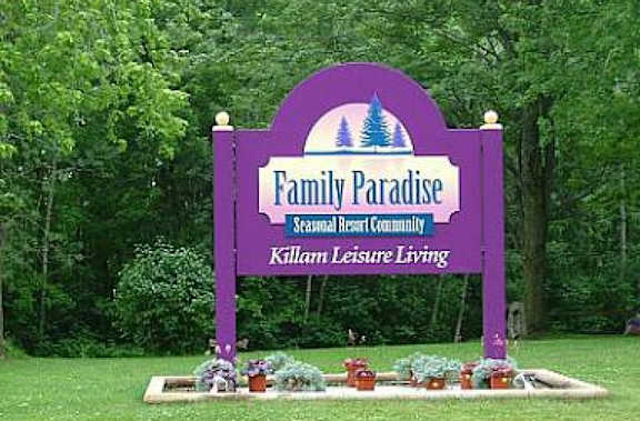 A sign welcoming people to Family Paradise with trees behind it