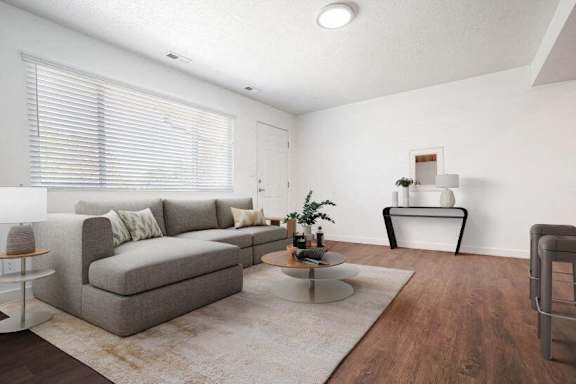 A living room with a grey couch, a glass table, and a plant.