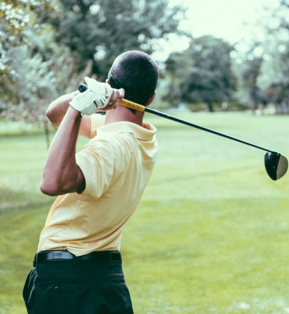 A man in a yellow shirt and black pants is swinging a golf club.