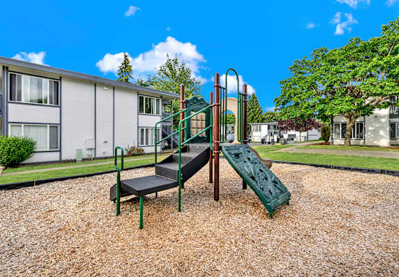 A playground with a green slide and a black mat.