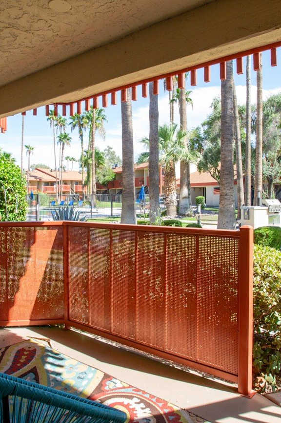 A red metal gate is in the foreground of a patio with a view of a park and palm trees.