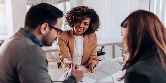 Three people are sitting at a table with papers, engaged in a discussion.