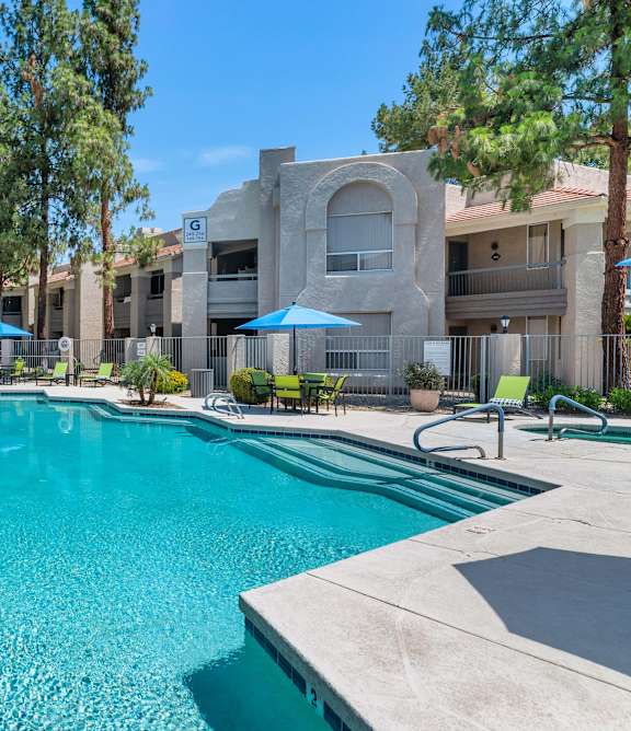A swimming pool surrounded by a concrete patio and a few trees.
