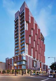 A tall red building with many windows is in the middle of a street.