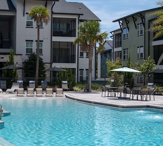 A swimming pool surrounded by lounge chairs and palm trees.