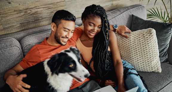a couple sitting on a couch with a dog and a laptop