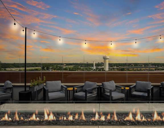 A fire pit sits in front of a row of chairs on a patio.