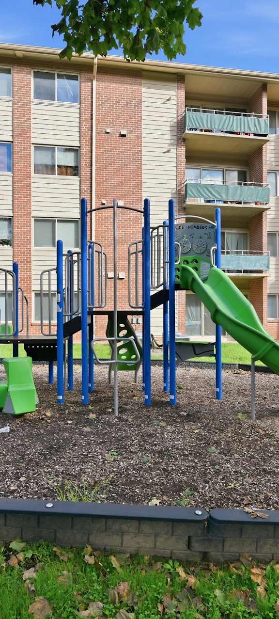 A playground with a green slide in front of a brick apartment building.