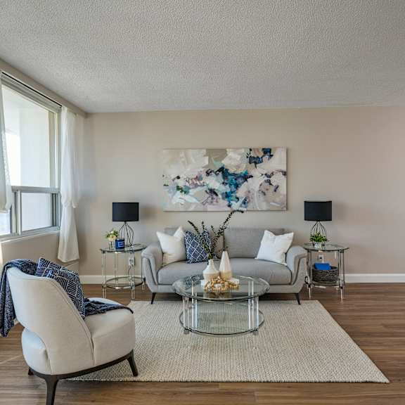 A living room with a white chair, a grey couch, and a glass coffee table.