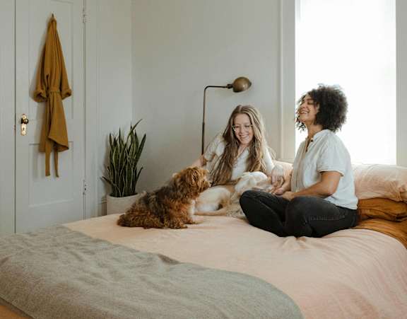 Two women sitting on a bed with a dog.