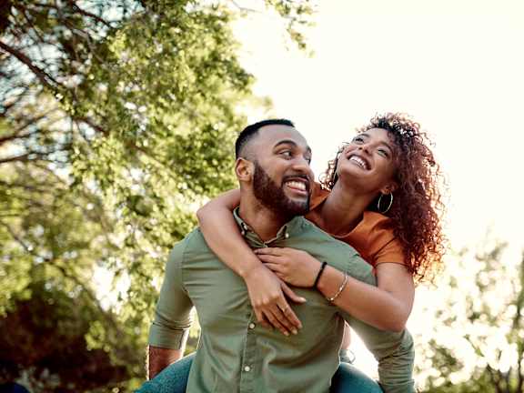 A man is carrying a woman on his back in a park.