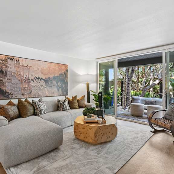 A living room with a grey couch and a large painting on the wall.