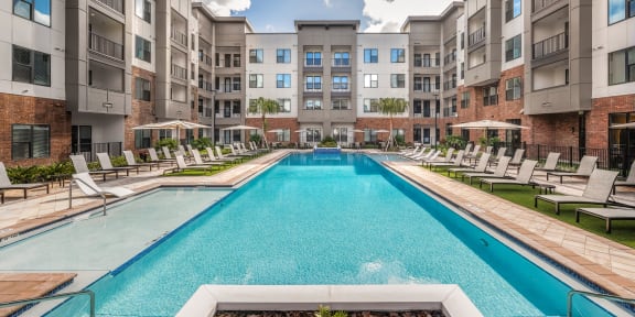 an apartment pool with chairs and an apartment building in the background at The Haven at Lake Britt Apartments, Winter Garden, FL 34787