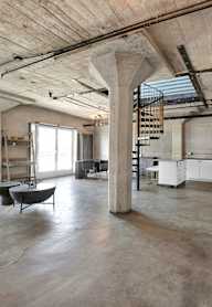 A large open space with a cement floor and a high ceiling with exposed pipes.
