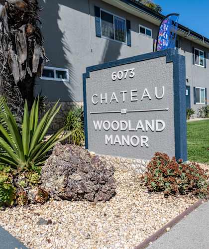 A sign for Chateau Woodland Manor is in front of a building.