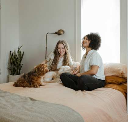Two women sitting on a bed with a dog.