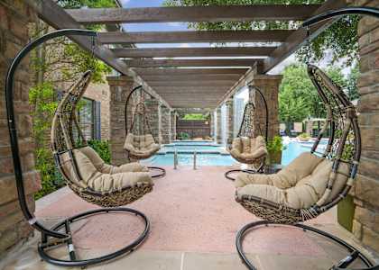 A patio with a pool and hanging chairs.