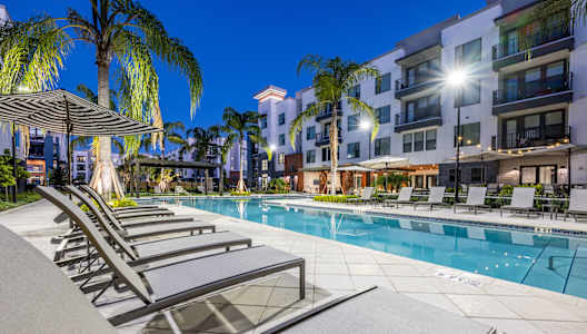 a swimming pool with lounge chairs at night at 19 South Apartments in Kissimmee, FL