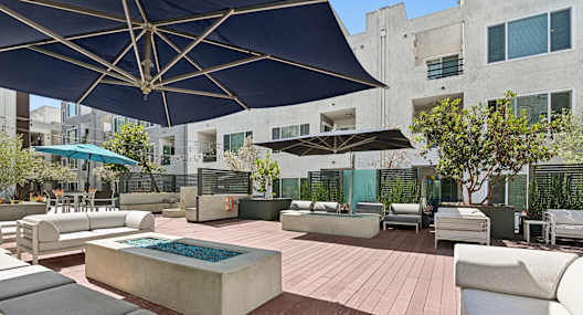 A patio with a pool and chairs under a blue umbrella.