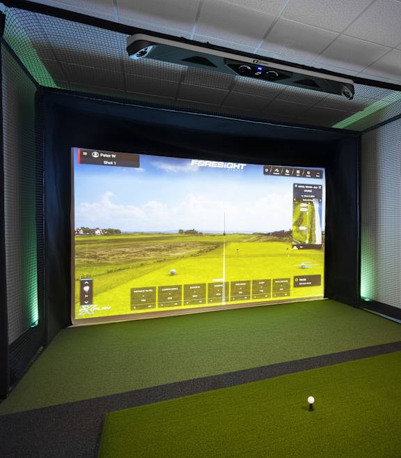 a room with a golf simulator and a screen on the wall