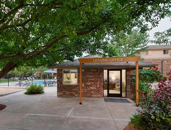A leasing office is surrounded by greenery and has a pool in the background.